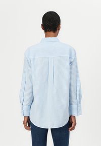 Camicia a righe blu e bianche con bottoni, dotata di spalle con yoke, maniche lunghe con polsini abbottonati e orlo curvo. Tessuto in misto cotone.