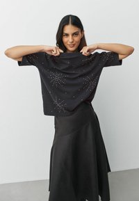 Zwarte shirt met korte mouwen met sterachtige versieringen in verschillende maten, gecombineerd met een zwarte A-lijn rok. Smooth stof textuur.