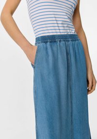 Jupe maxi en denim bleu clair avec une taille élastique et des poches latérales. Présente une texture lisse et une coupe décontractée.