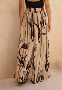 Pantalons larges fabriqués dans un tissu léger et texturé. Présente une base beige avec des motifs de feuilles marron foncé et des lignes verticales. Taille élastique.
