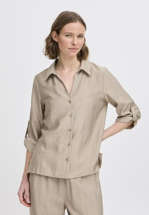 Beige košile na knoflíky s límcem a vyhrnutými rukávy. Vyrobena z texturované látky, má volný střih a decentní kapsy.