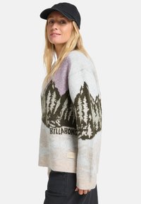 Pull en maille avec un motif de montagne dans des tons de vert, beige et lilas, doté un ourlet côtelé et d'une étiquette tissée en bas.