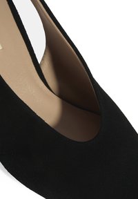 Chaussure slingback en daim noir à bout pointu, avec une découpe en V à l'avant et une doublure intérieure lisse.