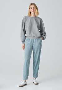 Felpa grigia con vestibilità rilassata, abbinata a pantaloni leggeri blu chiaro con texture e sneakers bianche. Materiali morbidi; vita elastica sui pantaloni.