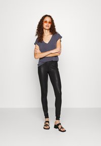 Grå V-halsad t-shirt, kort ärm; svarta leggings med ormmönster; svarta sandaler med remmar; oranga solglasögon. Enkelt och figurnära design.
