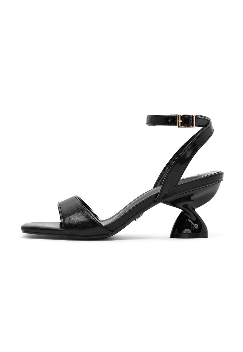 Musta korkokengät, joissa on kiiltävä pinta. Niissä on kaksi leveää remmiä, nilkkasolki ja ainutlaatuinen kaareva korkeakannan muoto.