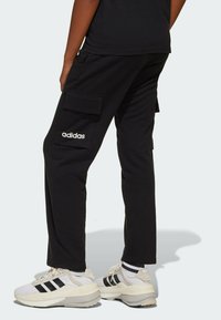 Svarta cargobyxor i bomullsmix, med sidfickor och en broderad vit Adidas-logga, matchade med vita och svarta skor.