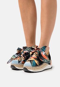 Chaussures colorées de style espadrille avec une tige en tissu à motifs, de grands nœuds, et une semelle enveloppée de jute avec une base en caoutchouc blanc.