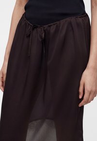 Μαύρη διάφανη φούστα με σούρα στη μέση, φορεμένη πάνω από μαύρη εσώφουστα, ορατά χέρια στα πλάγια και μαύρο ριμπ τοπ.