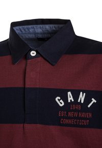 Poloshirt mit breiten horizontalen navyblauen und burgunderfarbenen Streifen, weißem Knopf und gesticktem Text "GANT 1949 EST. NEW HAVEN CONNECTICUT."