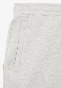 Pantalones deportivos gris claro con bolsillo lateral y cinturilla elástica, mostrando la textura de la tela y una pequeña etiqueta de marca beige en el lado izquierdo.