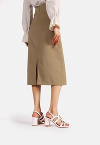 Gonna midi khaki con spacco sul retro, abbinata a sandali bianchi con tacco alto a blocco e cinturino alla caviglia regolabile.