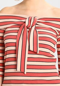 Off-shoulder top i ribbet stof med koral- og cremegule vandrette striber, med en knyttet frontdetalje og trekvartlange ærmer.