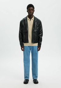 Czarna skórzana kurtka zapinana na zamek z dwoma przednimi kieszeniami, beżowy top z kołnierzykiem pod spodem, jasnoniebieskie dżinsy o prostych nogawkach i czarne buty.