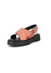 Sandal in pelle arancione con borchie argento, design open-toe, cinturino alla caviglia regolabile e una spessa suola in gomma nera con texture a righe.