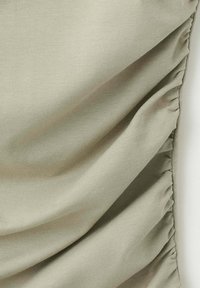 Tissu vert clair avec un détail de couture froncée le long d'un bord, créant des plis doux et une texture.