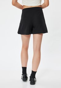 Pantaloni corti neri con una texture liscia, vestibilità rilassata e orlo svasato, abbinati a scarpe e calze nere per un look coordinato.