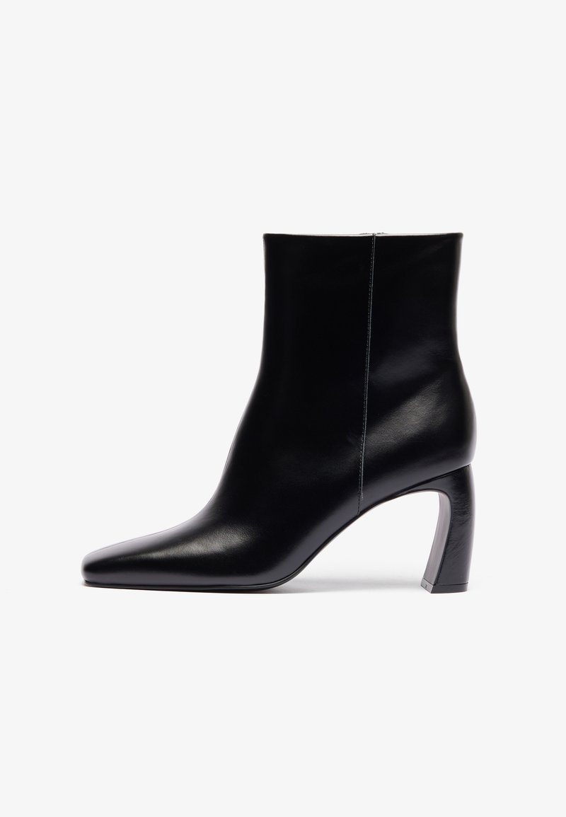 Black leather ankle boot with a pointed toe, slim silhouette, and curved high heel featuring a metallic accent at the base.