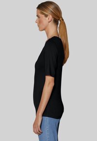 Schwarzes kurzärmeliges Oberteil aus weichem Stoff mit Rundhalsausschnitt und figurbetonter Silhouette, kombiniert mit hellblauen Jeans.