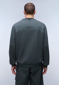 Donkergroene sweatshirt met een ronde hals, geribbelde manchetten en zoom. Glad oppervlak en subtiele naaddetails op de rug.