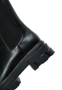 Botte de cheville en cuir noir avec panneau latéral élastique, semelle en caoutchouc texturé et semelle épaisse pour une meilleure adhérence et durabilité.