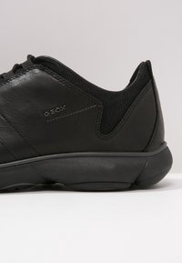 Black athletic shoe with leather and mesh materials. Features a rubber sole, subtle GEox branding, and a streamlined design.