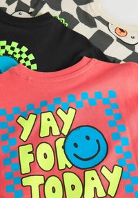 Drei T-Shirts: eines in Pink mit "JUCHU FÜR HEUTE" in fettem Gelb und blauem Smiley, eines in Schwarz mit grünem Karomuster und eines in Grau mit Tiergrafik.