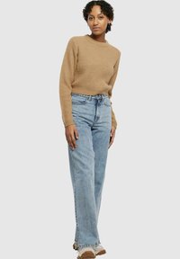 Light brown textured knit sweater with a round neckline, paired with light blue straight-leg jeans and beige sneakers. Simple, casual outfit.