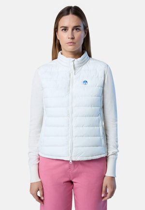 Gilet bianco trapuntato con colletto alto, chiusura con zip e piccolo logo blu sul petto. Indossato sopra una maglietta a maniche lunghe di colore chiaro.
