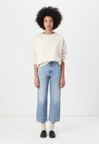 Beige Oversized-Pullover mit langen Ärmeln, kombiniert mit geraden Jeans in mittlerem Waschung und schwarzen Schuhen mit beigen Socken.