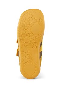 Żółta podeszwa buta dziecięcego z teksturowanymi, okrągłymi wzorami oraz małą wytłoczoną postacią w pobliżu obszaru podbicia stopy.