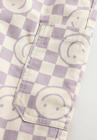 Taschen aus helllila und cremefarbenem kariertem Stoff mit einem Muster von lächelnden Gesichtern, sichtbaren Nähten und einem taillierten Rand.