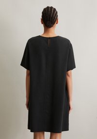 Black short-sleeve dress with a loose fit, featuring a back keyhole closure and smooth texture. Simple design without patterns or embellishments.