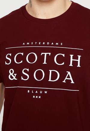 T-shirt en coton bordeaux arborant un texte blanc audacieux avec le nom de la marque "SCOTCH & SODA" et "AMSTERDAMS BLAUW" dans un design centré.
