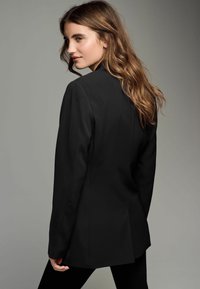Must mustrakk blazer struktureeritud õlgadega, sile tekstuur, ühe nupuga kinni, klassikaline lõige, stiilitud kitsaste pükstega.