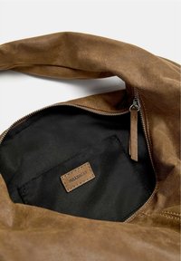 Brown leather shoulder bag with a zip closure, featuring a black fabric interior and a small branded tag. Soft, textured exterior.