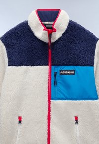 Fleece jacket with navy upper, creamy lower, and bright blue chest pocket. Features red zipper and accents. Textured, soft fabric.
