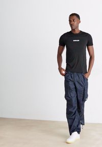 Black short-sleeve T-shirt with a white logo, paired with navy cargo pants featuring side pockets, and white sneakers. Minimalist design.