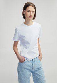 Camiseta blanca de algodón con mangas cortas, escote redondo y silueta ajustada, combinada con jeans de mezclilla azul claro con estampado.