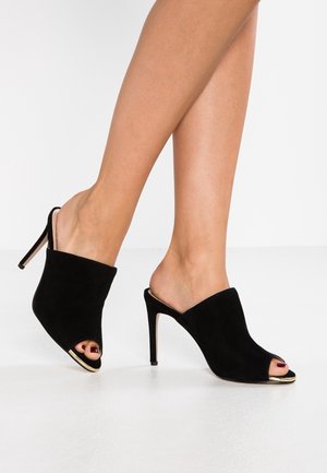 Zwarte suède open teen muilen met een stijlvolle hoge hak en gouden accent op de zool. Gladde textuur en minimalistisch ontwerp.