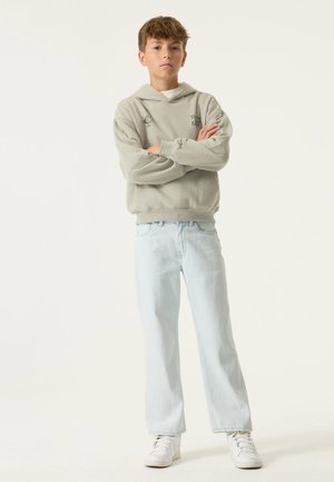 Hellgrauer Hoodie mit Kängurutasche, kombiniert mit hellblauen Jeans mit geradem Bein und weißen Sneakers. Weiche Textur und lässige Passform.