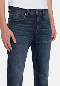 Jeans in denim blu scuro con una vestibilità slim, caratterizzati da leggere sfumature, cuciture arancioni e un design classico con chiusura a bottoni.