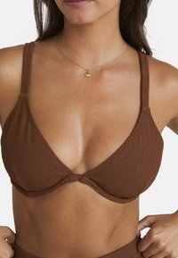 Braunes geripptes Bikini-Top mit verstellbaren Trägern und einem Knoten-Detail in der Mitte. Das Material ist strukturiert und sorgt für ein dezentes visuelles Interesse.