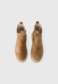 Une paire de bottines en daim beige avec des bouts ronds et des semelles texturées claires sur fond blanc.