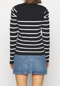 Schwarz-weiß gestreifte langärmelige Bluse mit gerippter Textur, kombiniert mit einem Denim-Minirock mit zwei Gesäßtaschen.