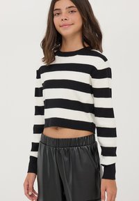 Maglione a righe in bianco e nero, corto, con maniche lunghe, texture a coste e scollo rotondo, abbinato a pantaloni corti neri con vita elastica.