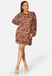 Korte jurk met lange moutjes in een wervelend oranje en donkerbruin zebra-patroon; losse pasvorm, ronde halslijn en elastische taille detail.