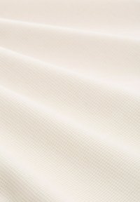 Getextureerde witte stof met een subtiel geweven patroon, gedrapeerd in zachte plooien, met een zachte, gladde afwerking en een lichte glans.