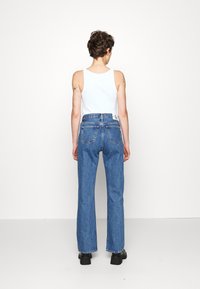 Siniset farkut korkealla vyötäröllä, suora lahje, näkyvät ompeleet ja kaksi takataskua, yhdistetty valkoiseen toppiin.