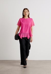 Rosa kortärmad topp med peplumkant, i kombination med svarta högmidjade byxor och svarta spetsiga klackskor. Enkel design, lättviktig tyg.